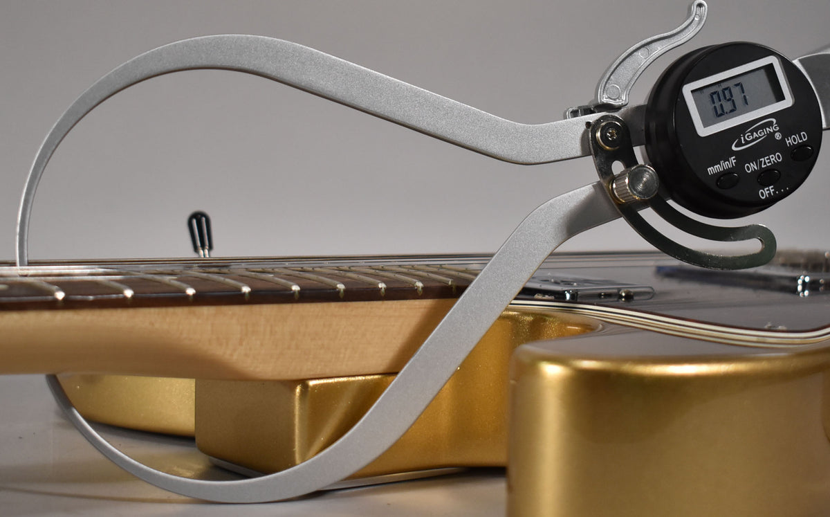 A digital caliper measures the string height above the frets on a gold Telecaster's maple neck, displaying "0.97".