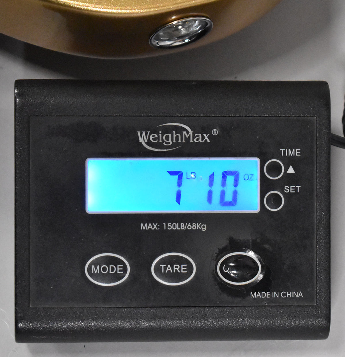 A black digital scale displays "7 LBS 10 OZ" in blue, with a gold guitar body and chrome jack plate visible above.