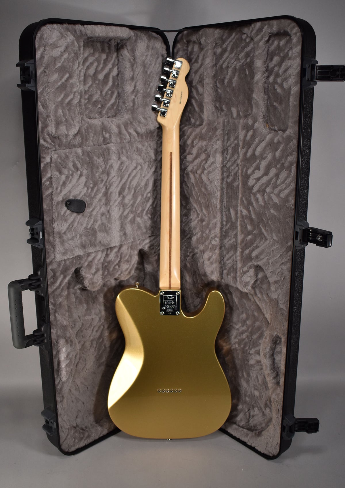 The back of a metallic gold Telecaster with a light maple neck and chrome tuners, resting in a plush-lined hard case.