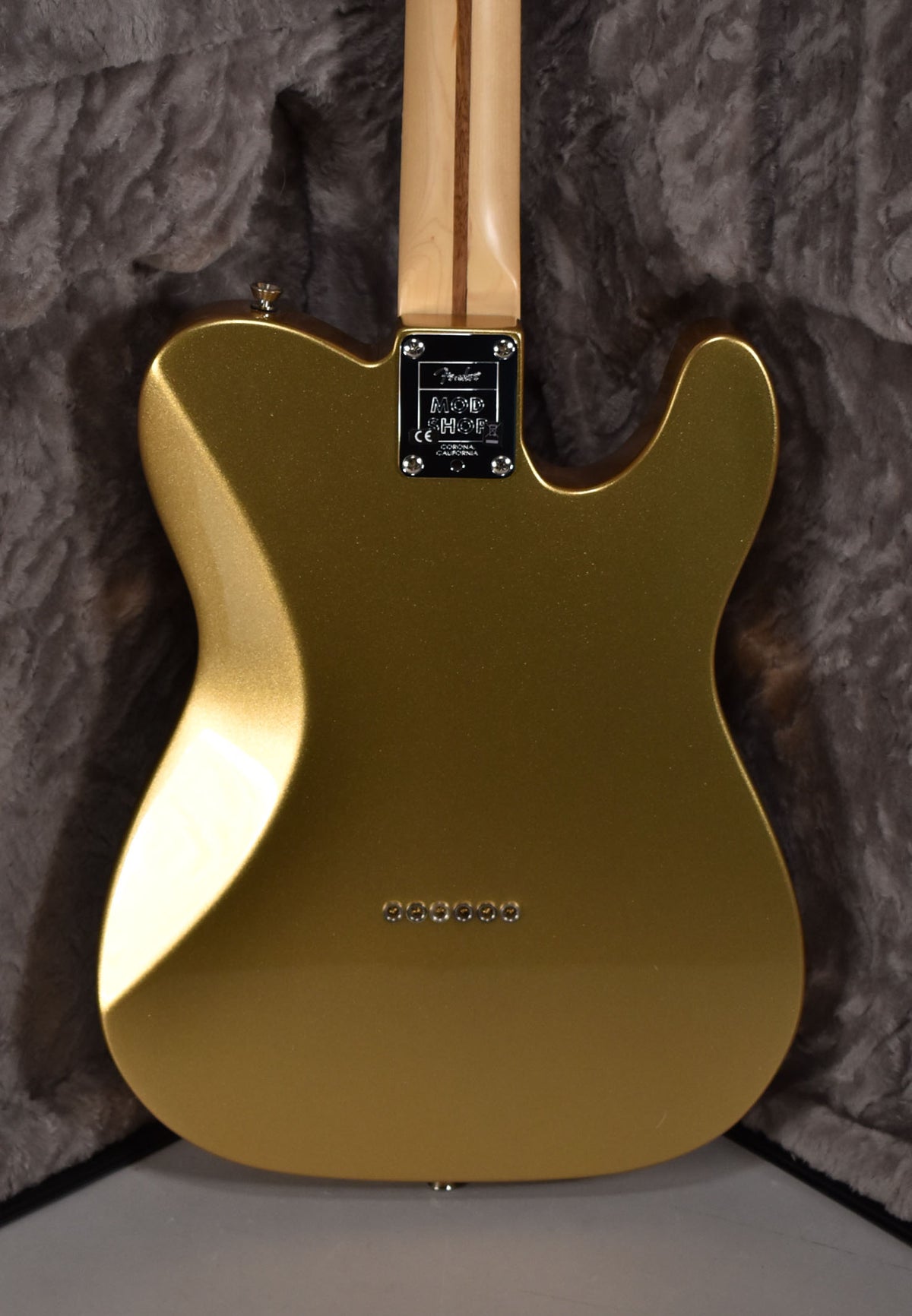 The back of a metallic gold Telecaster, showing the neck plate, six string-through-body ferrules, and a light wood neck.