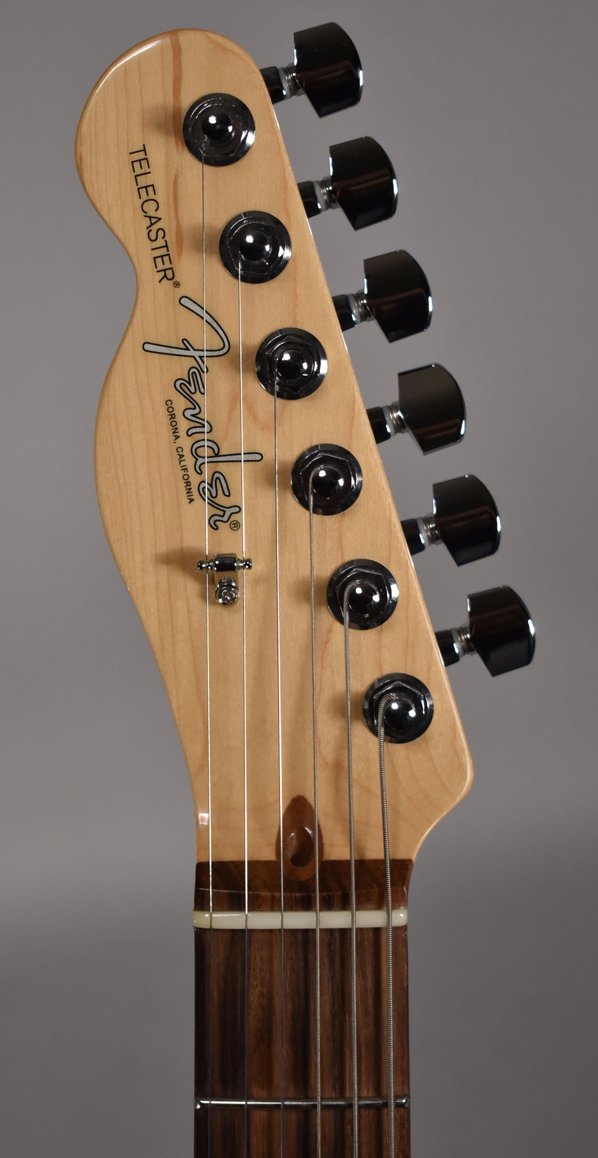 Close-up of the light wood headstock with six black tuners, a string tree, and a dark wood fretboard with a white nut.
