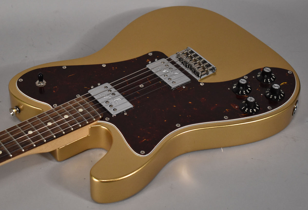 The left-handed gold Telecaster is angled from the neck, showing its tortoiseshell pickguard, two chrome humbuckers, and four black control knobs.
