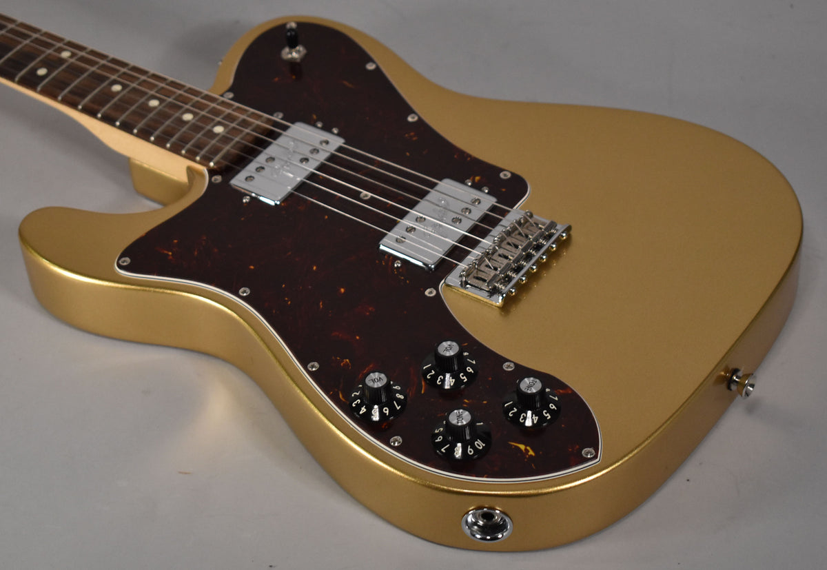 A left-handed gold Telecaster with a tortoiseshell pickguard, two chrome humbuckers, and four black control knobs.