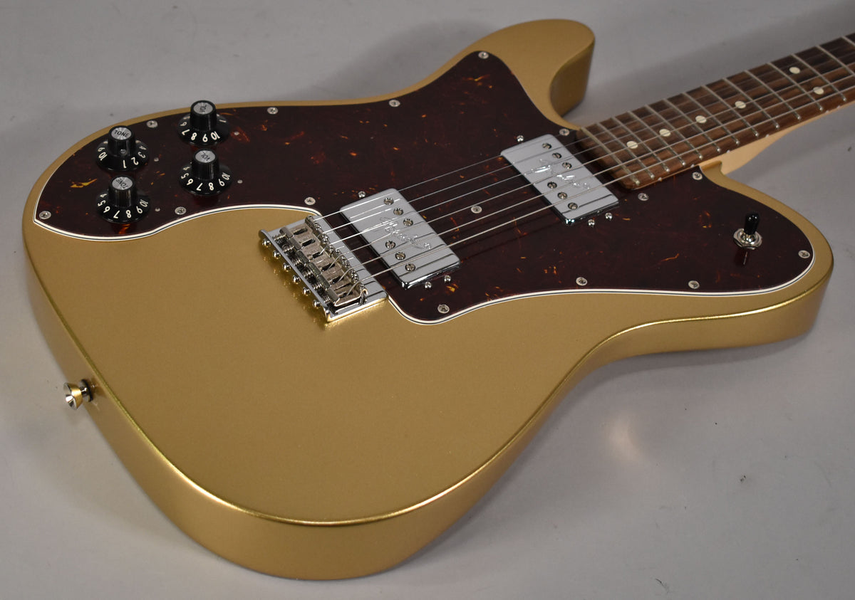 Left-handed gold guitar, angled from above, showing the body with a tortoiseshell pickguard, chrome humbuckers, and four black control knobs.