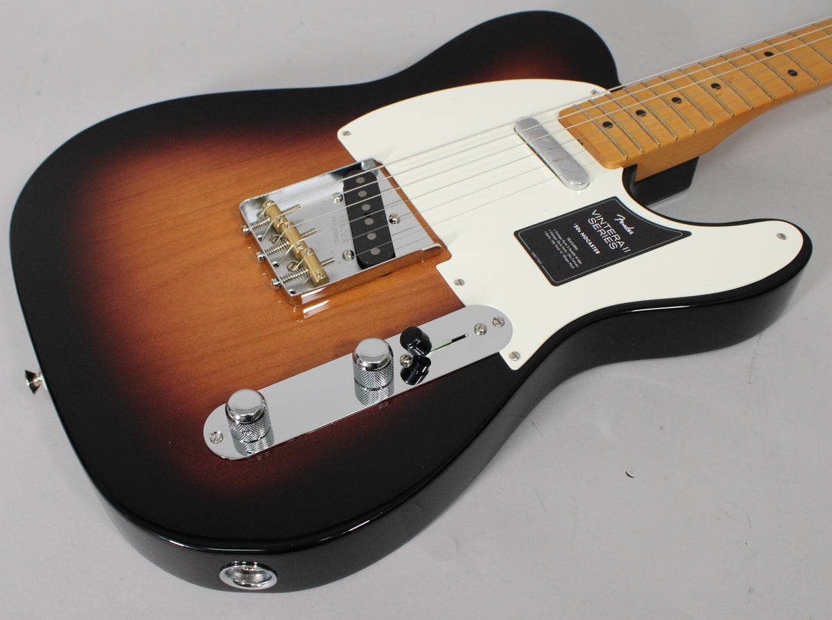 The sunburst electric guitar is angled from the lower right, showing its glossy body, white pickguard, and chrome bridge with brass saddles.