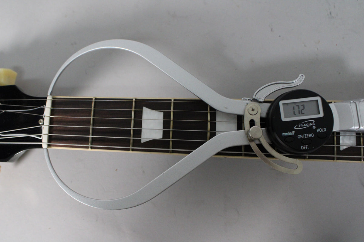 A digital caliper measures the nut width of the dark fretboard with trapezoid inlays, showing 1.72 inches.