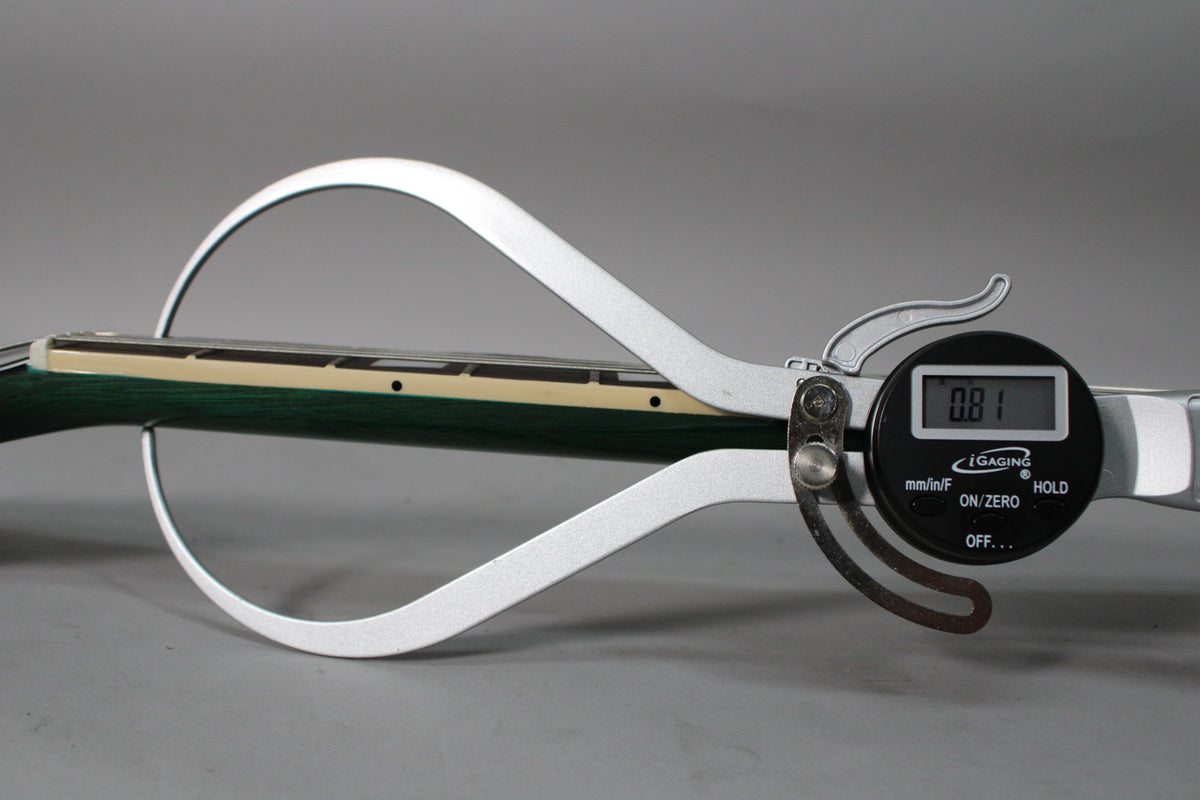 A digital caliper measures the neck thickness of the translucent teal guitar, showing 0.81 on its display.