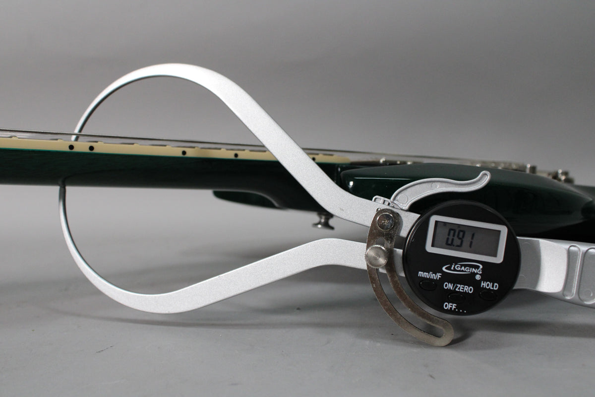 A digital caliper measures the neck of a translucent teal guitar, displaying "0.91".