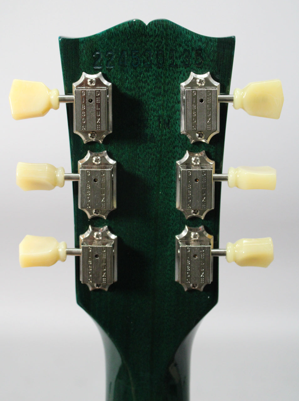 The back of the translucent teal headstock, showing six cream-buttoned tuners with nickel housings, and a faint serial number.