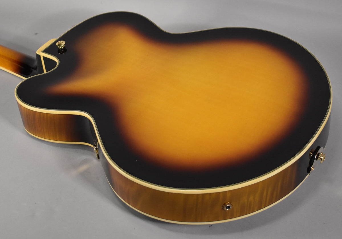 The archtop guitar's glossy sunburst back and sides are visible, with a gold strap button near the neck heel and a chrome output jack.