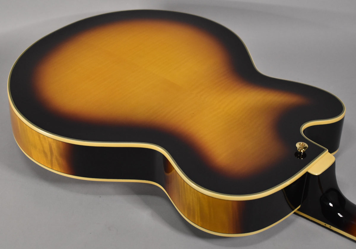 The guitar's sunburst back, with visible wood grain, curves into the dark sides, featuring cream binding and a gold strap button.
