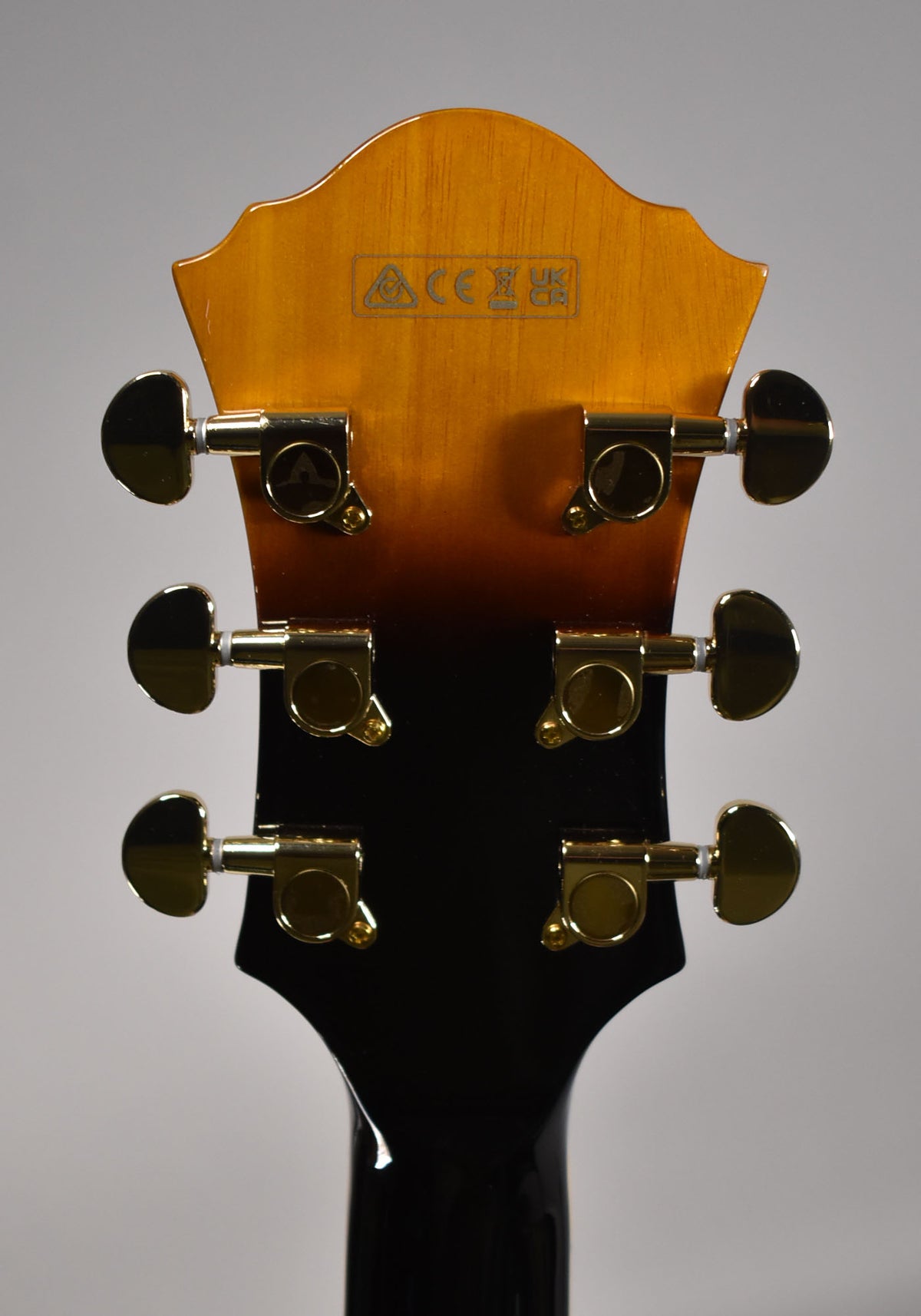 Rear view of the guitar's headstock, showing a sunburst finish fading to black, with six gold-plated tuning machines.