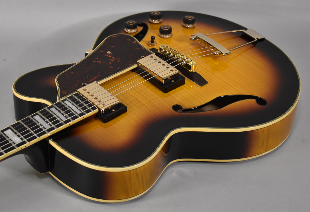 Close-up of the sunburst archtop guitar's body, showing gold hardware, f-hole, tortoise pickguard, and cream binding.