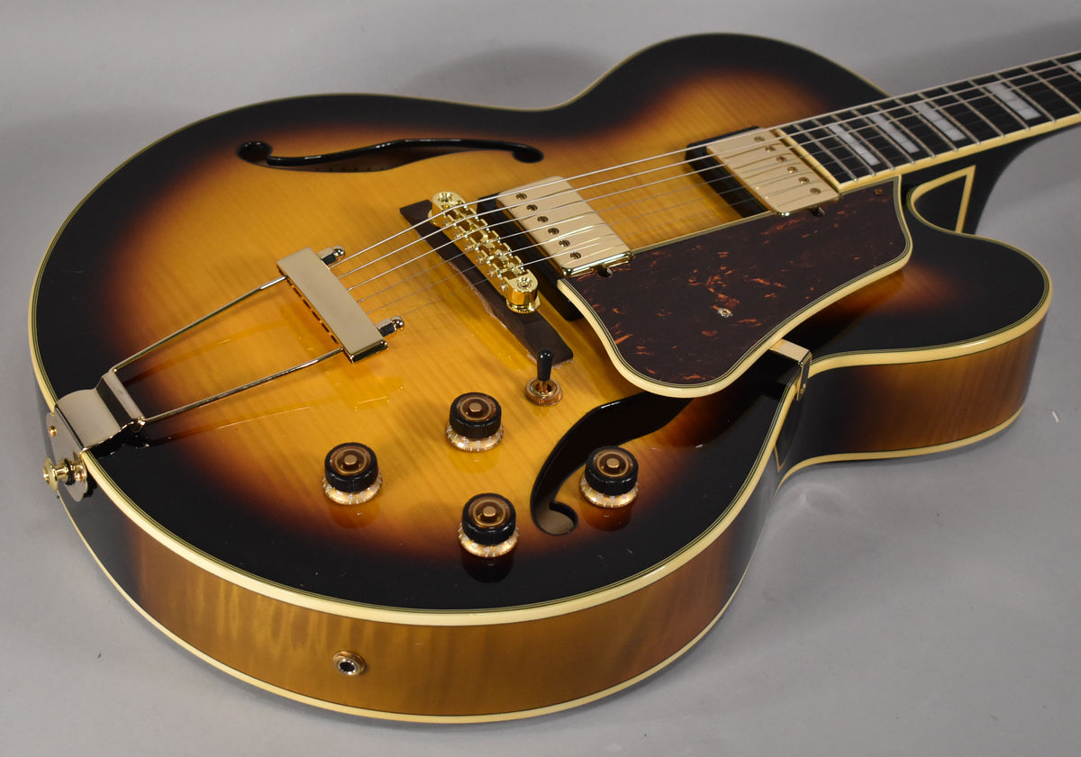 The sunburst archtop's body is angled from the lower left, showing gold hardware, four amber control knobs, and a tortoiseshell pickguard.
