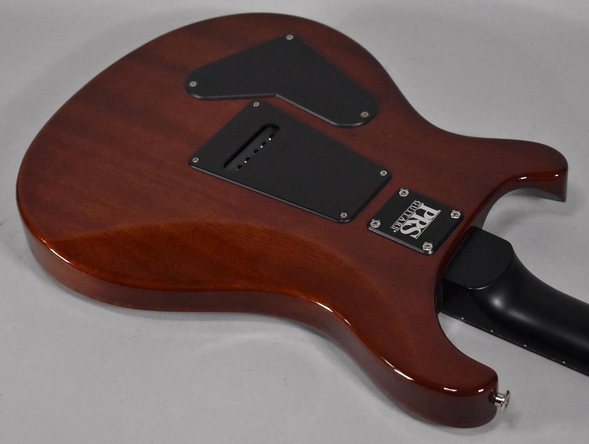 The guitar's glossy reddish-brown back, angled from the lower bout to the upper horn, shows black control cavity covers.