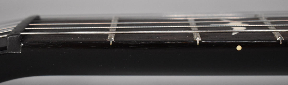 Close-up of the guitar's dark fretboard and neck, showing the nut, frets, strings, and a cream side dot marker.