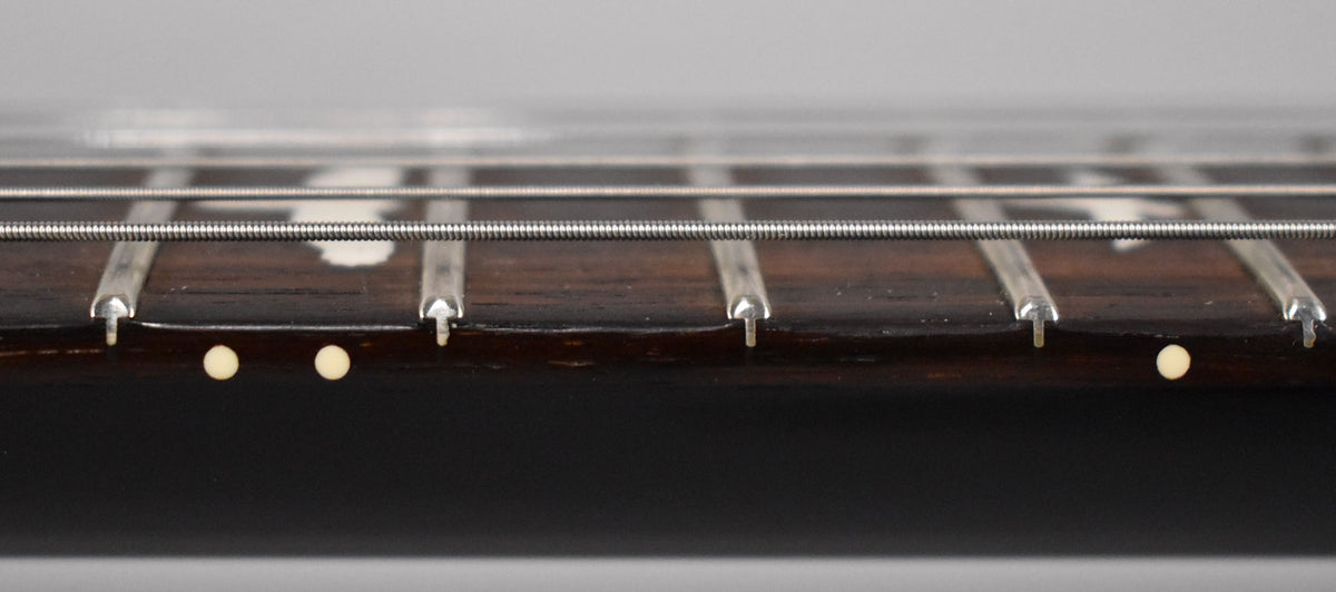 Close-up of the guitar's dark rosewood fretboard and frets, showing three light-colored side dot markers and four strings.