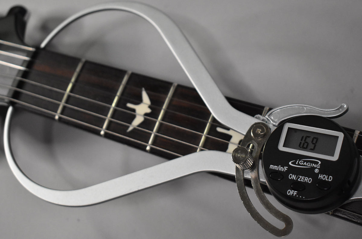 A digital string action gauge measures 1.69mm on the guitar's dark rosewood fretboard with bird inlays.
