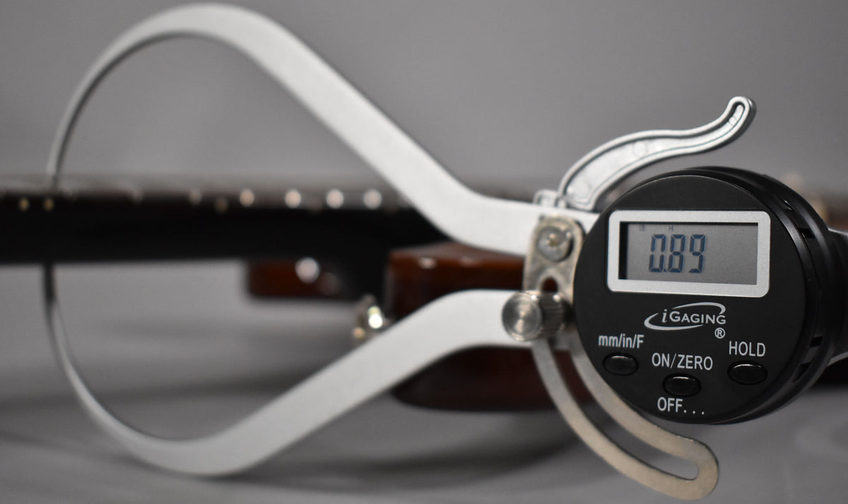 A digital caliper measures the guitar's dark brown fretboard, displaying "0.89" on its screen.