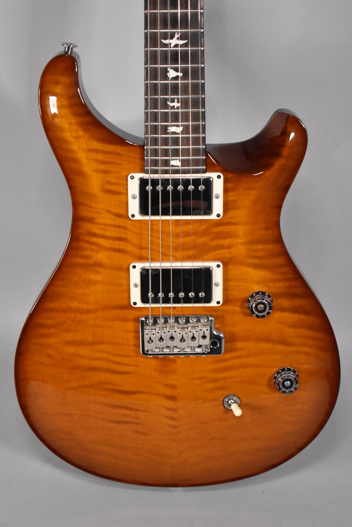 The guitar's flamed maple top has a glossy amber burst finish, with white bird inlays on the dark fretboard.
