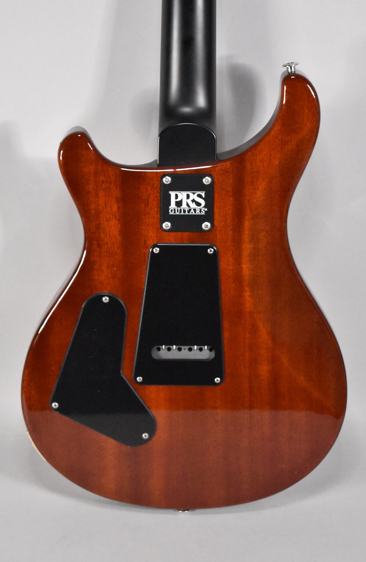The back of a glossy, dark reddish-brown guitar with a black neck, black control covers, and a black tremolo spring cover.