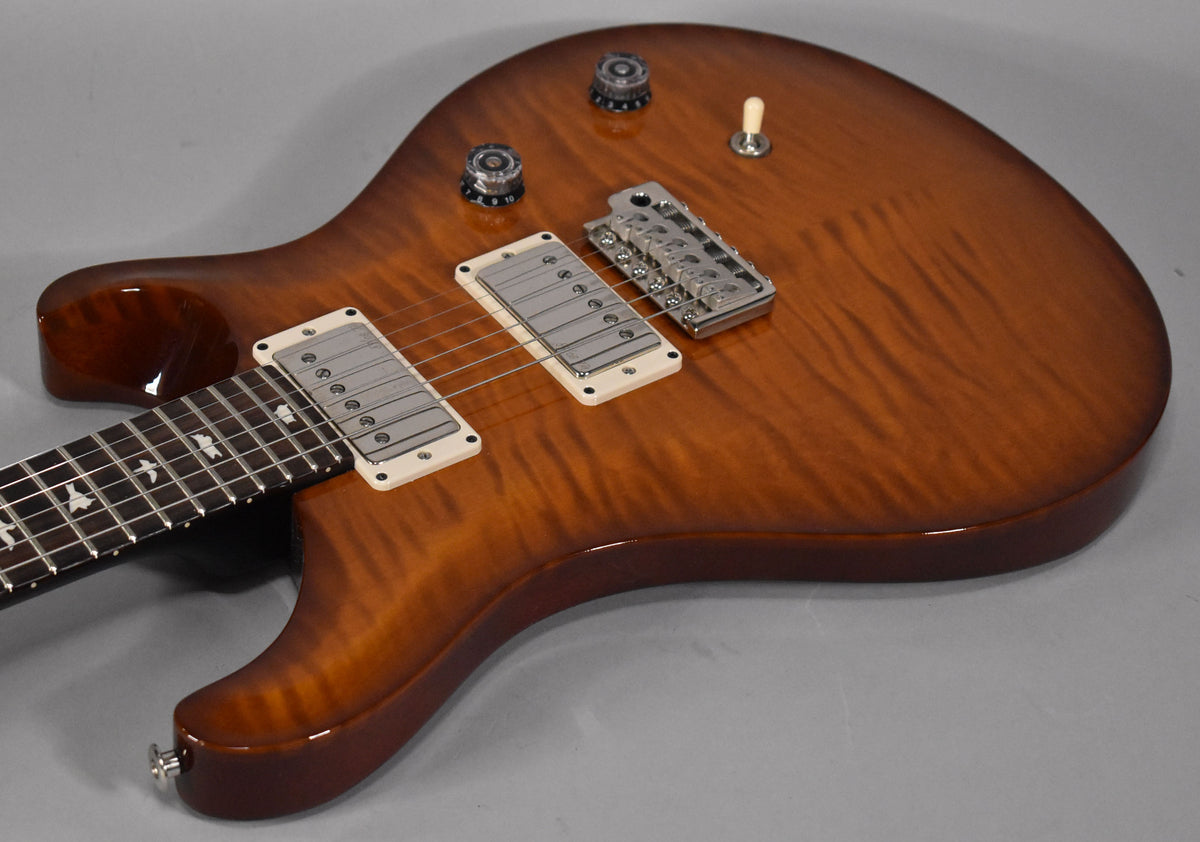 Close-up of a glossy brown burst electric guitar with flame maple top, two humbuckers with cream surrounds, and a chrome bridge.