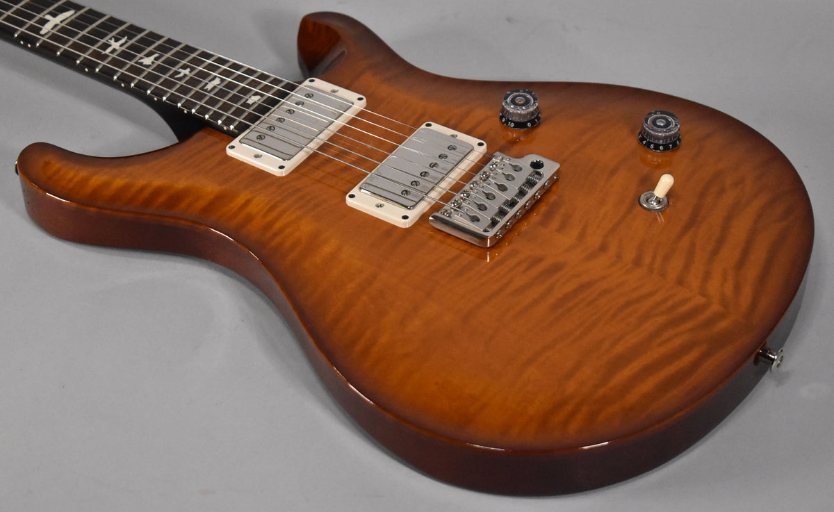 The guitar's body, angled from the neck, shows a glossy, flamed maple top in a rich amber burst, with two humbuckers and a tremolo bridge.