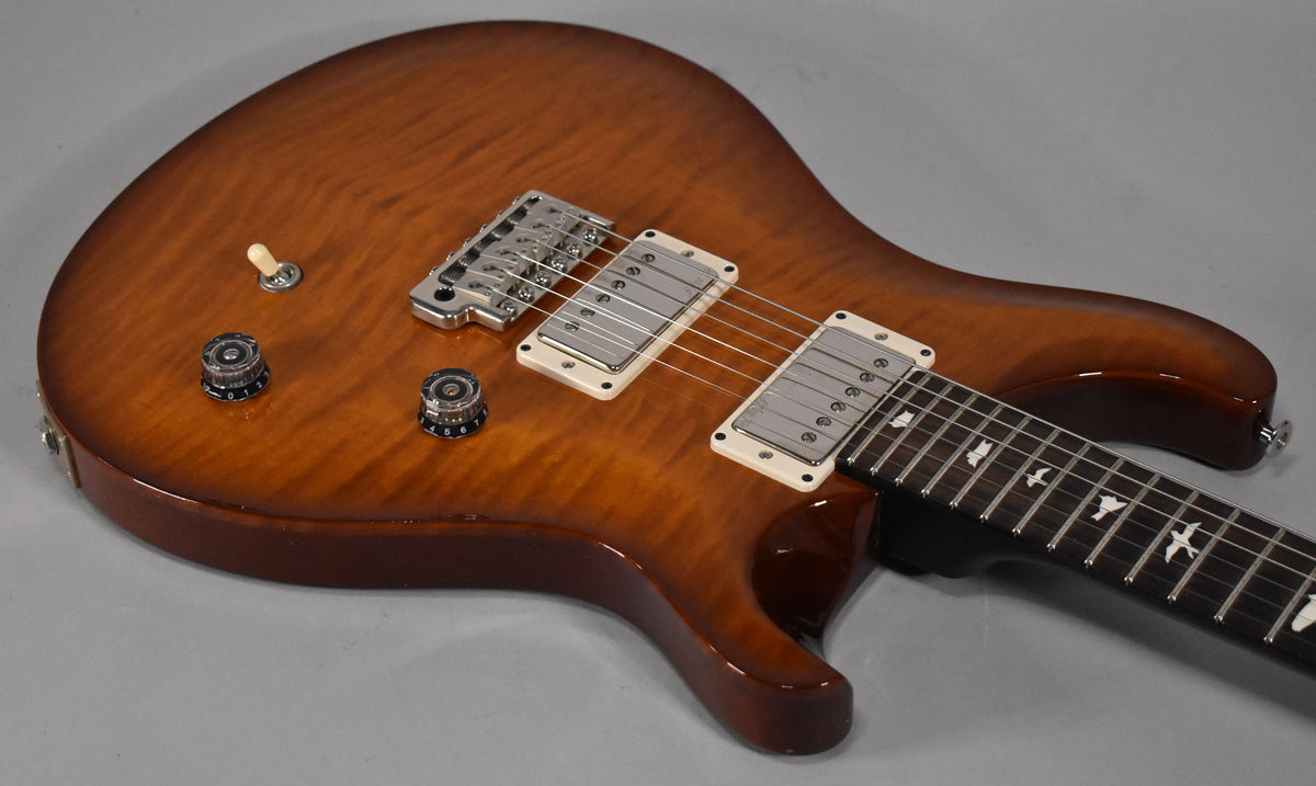 The electric guitar's flame maple top has a warm brown sunburst finish, with two humbuckers and bird inlays on the fretboard.
