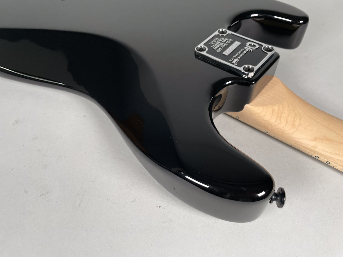 The guitar's glossy black body, with a chrome neck plate and a black strap button, meets a light wood neck.