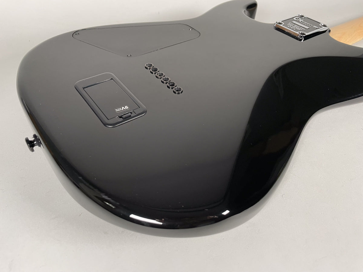 The guitar's glossy black back, angled from the lower bout, shows a battery compartment and six string-through-body ferrules.