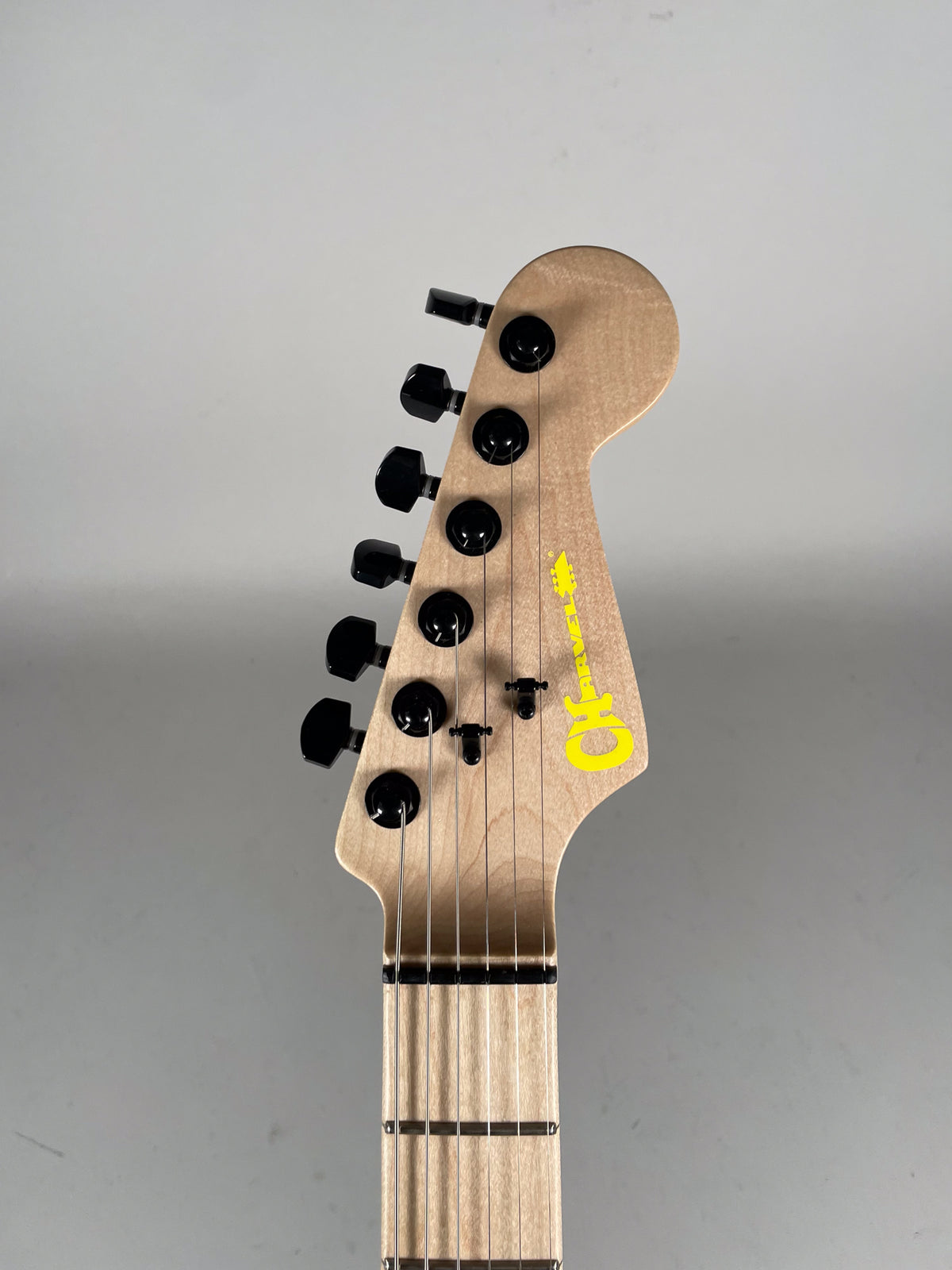 Close-up of the natural wood headstock with black tuners and a bright yellow logo, showing the top of the fretboard.