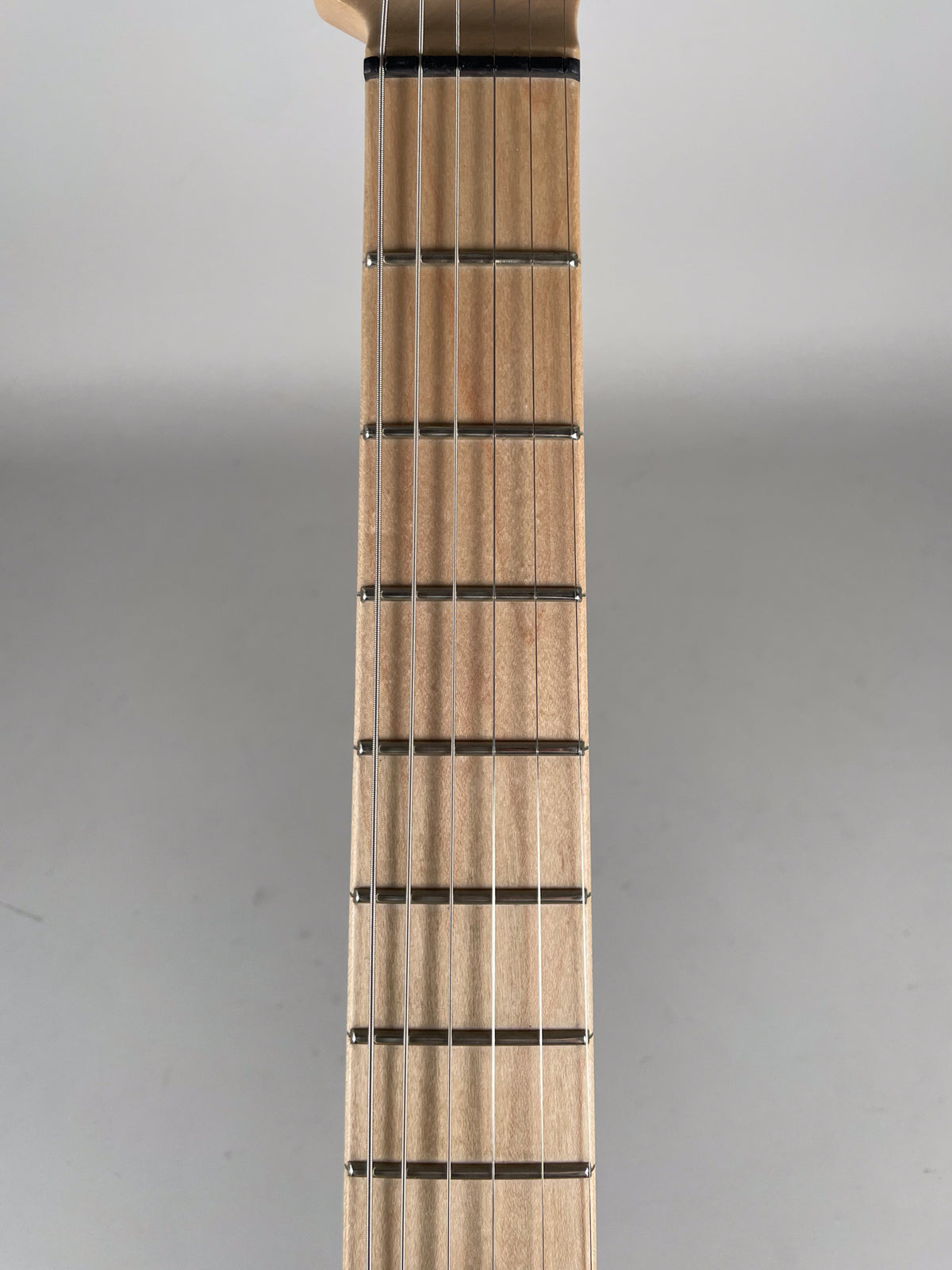 Close-up of the guitar's light wood fretboard with six strings and dark frets, viewed from the nut down to the sixth fret.