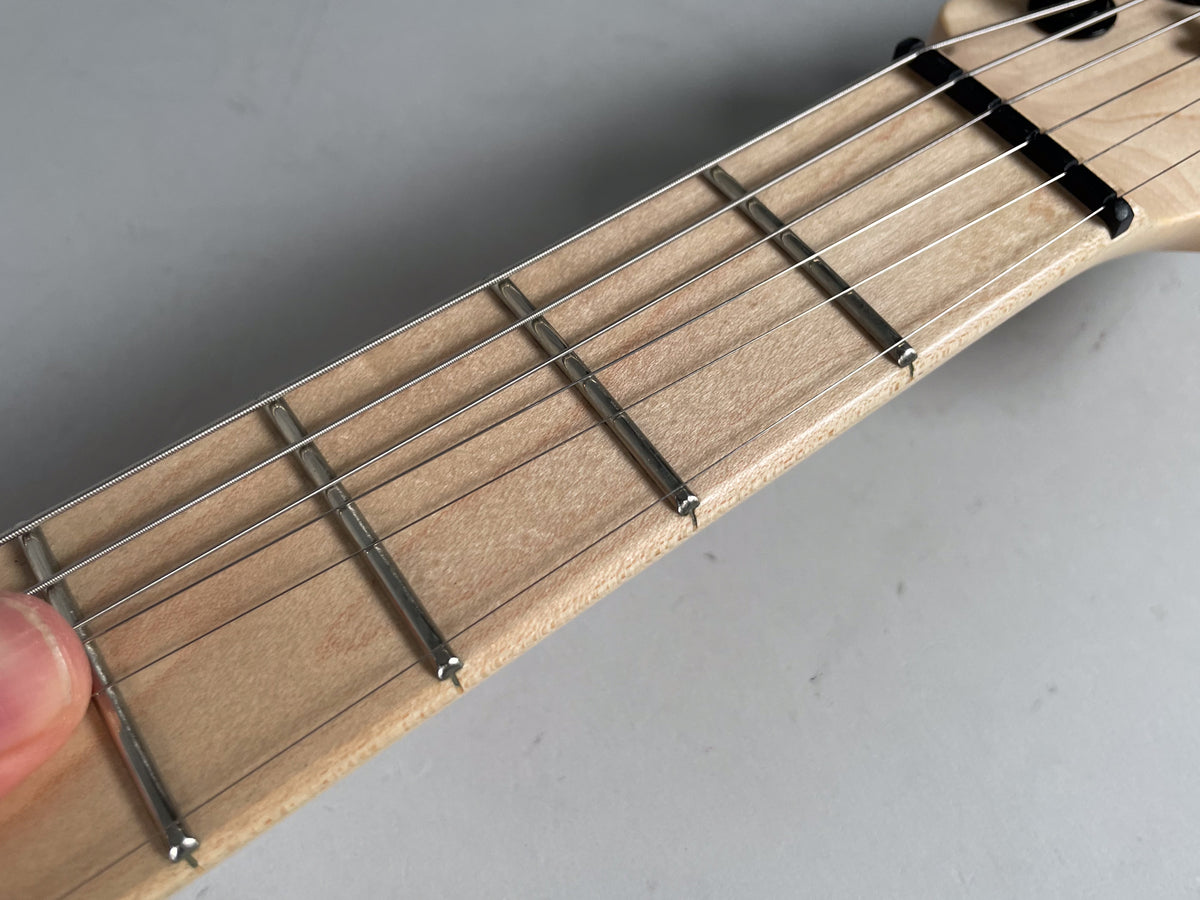 Close-up of the light wood fretboard and frets, with a black nut and strings, viewed from above at an angle.