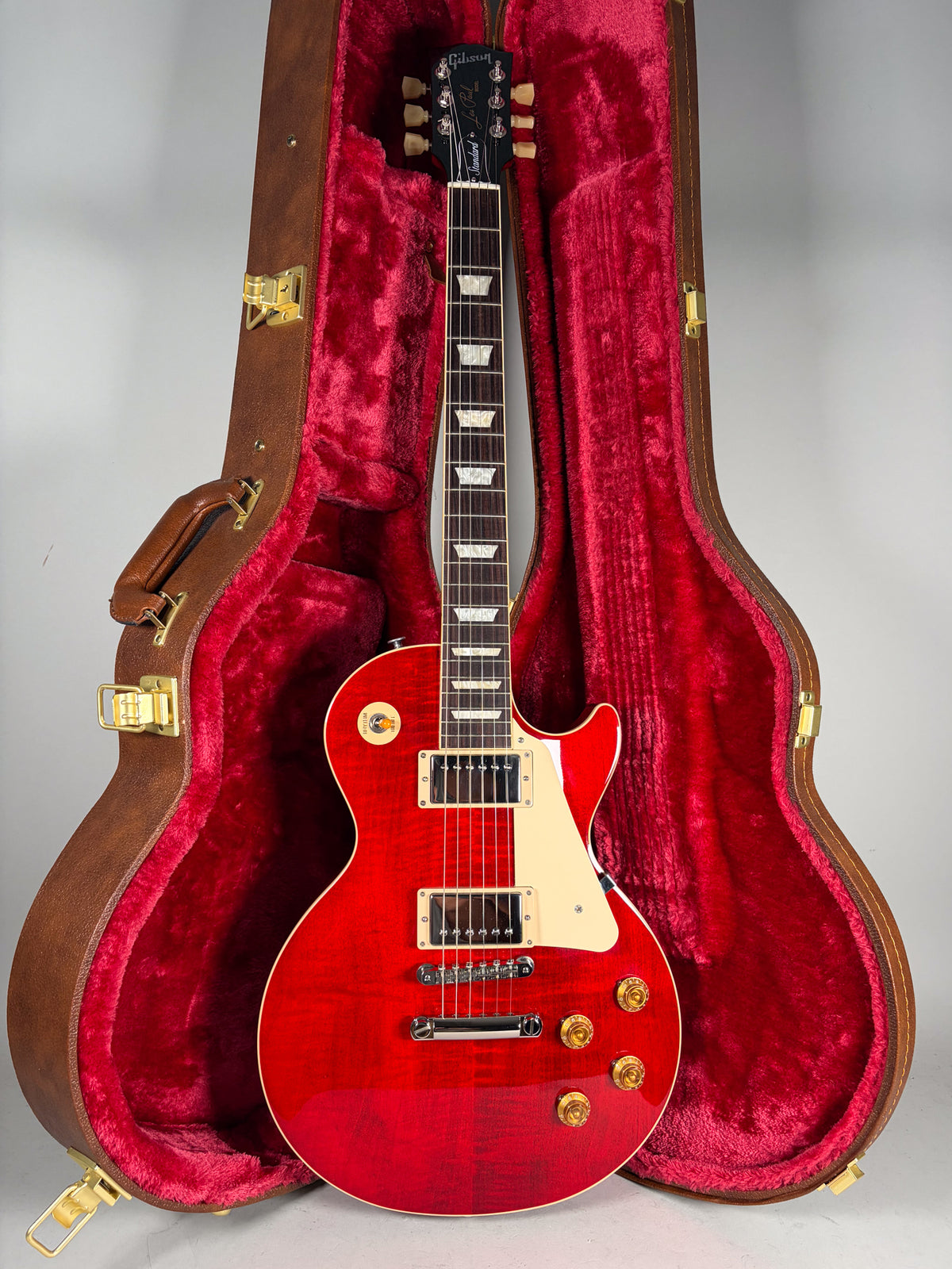 Full-length view of a cherry sunburst flame top Les Paul with cream binding, pickguard, and pickup rings, standing in its open brown case with red plush lining.