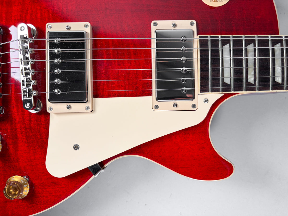 Close-up of a cherry red Les Paul's lower bout, showing two humbuckers, a cream pickguard, and gold control knobs.