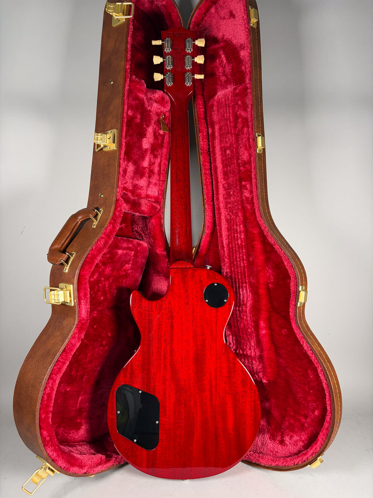 The back of a cherry red Les Paul with a visible wood grain, in a brown hard case with red plush lining.