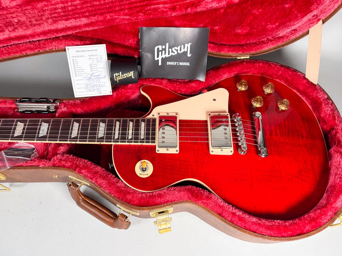A cherry red Les Paul with a flame top, cream pickguard, and gold top hat knobs, resting in its red-lined hard case.