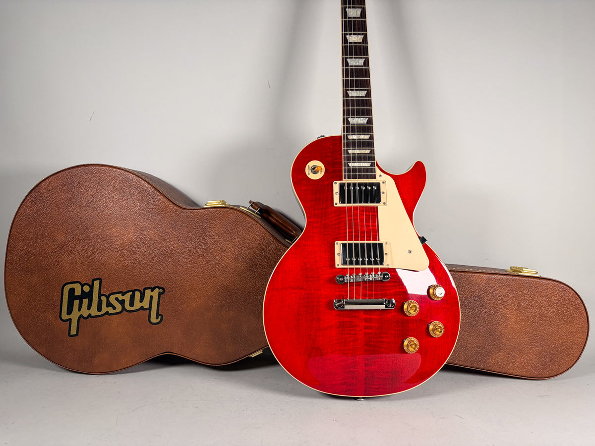 Full-body view of a cherry sunburst flame-top Les Paul with cream binding, pickguard, and gold hardware, next to its brown hard case.