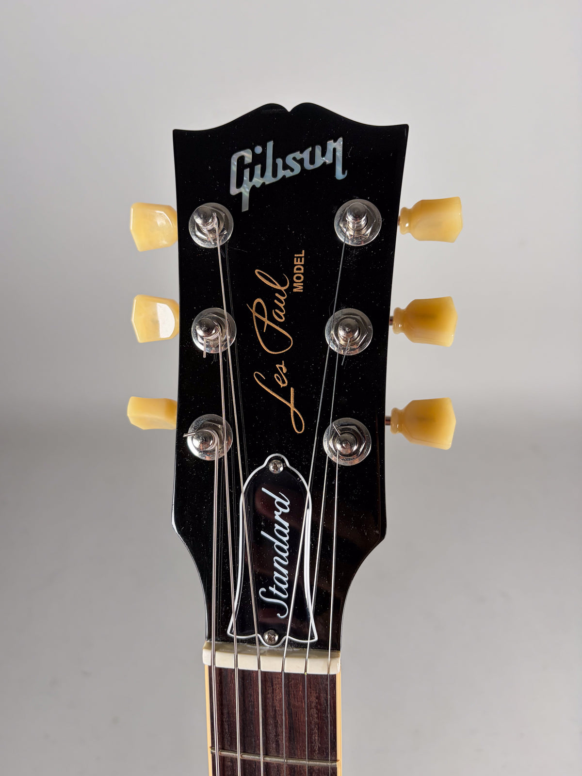 Close-up of a glossy black headstock with cream tuning pegs, chrome string posts, and a white bell-shaped truss rod cover.