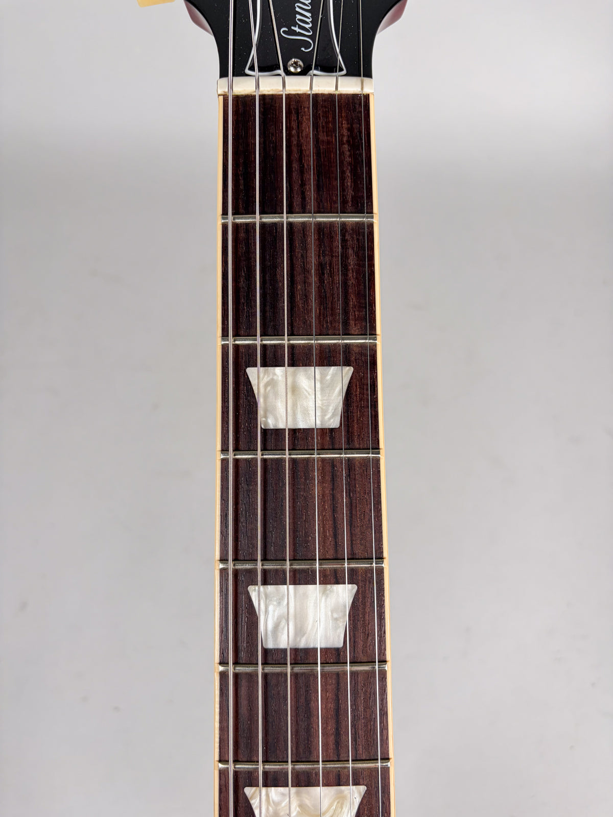 Close-up of the dark rosewood fretboard with trapezoid mother-of-pearl inlays, from the nut to the 12th fret.
