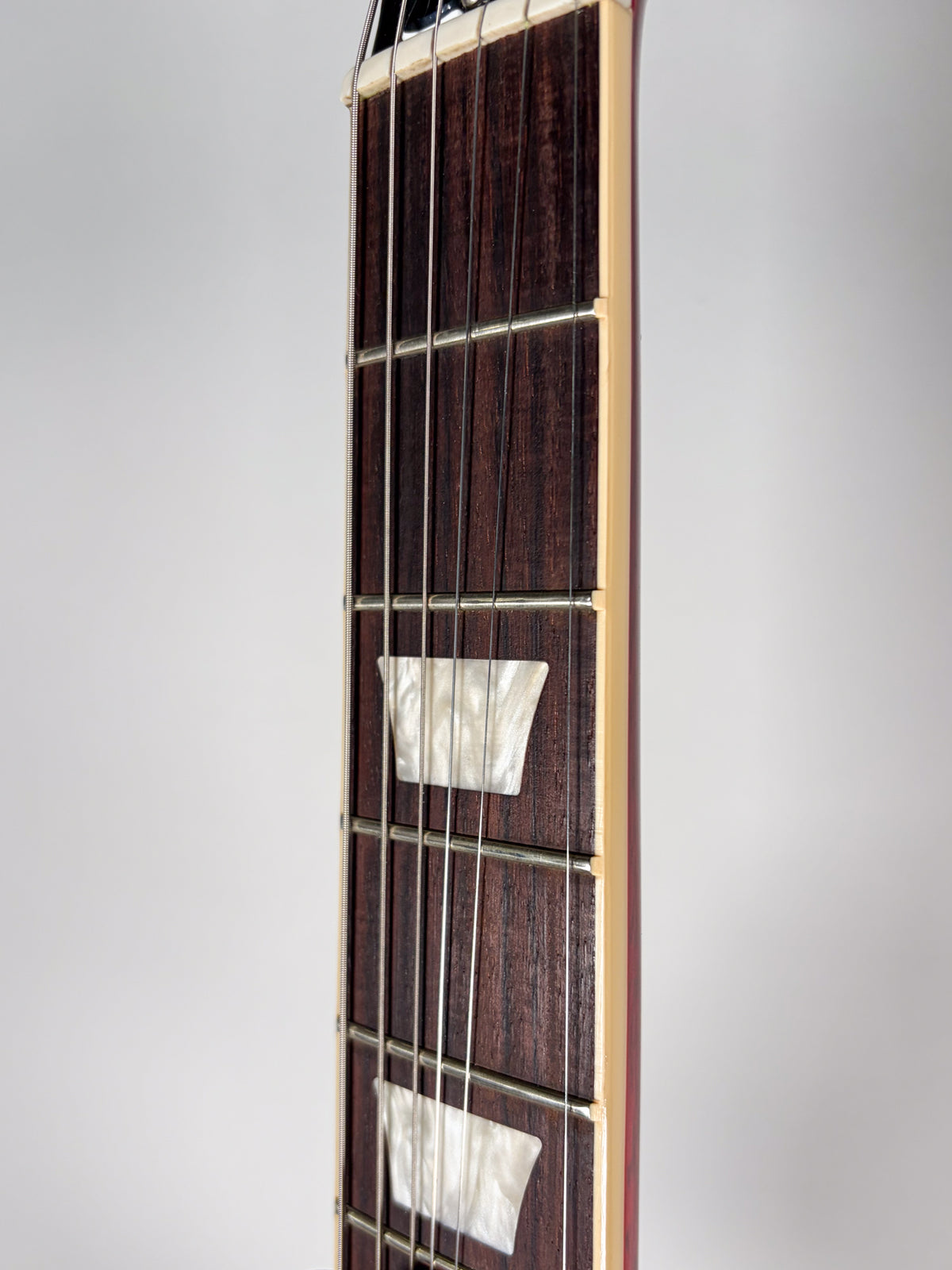 Close-up of the dark rosewood fretboard with trapezoid mother-of-pearl inlays, showing the frets and strings from the nut down.