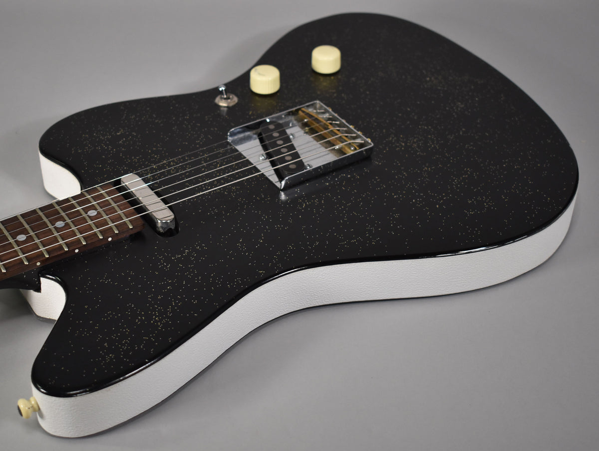 Close-up of a black sparkle guitar body with white textured sides, showing two cream knobs, a toggle switch, and chrome pickups.