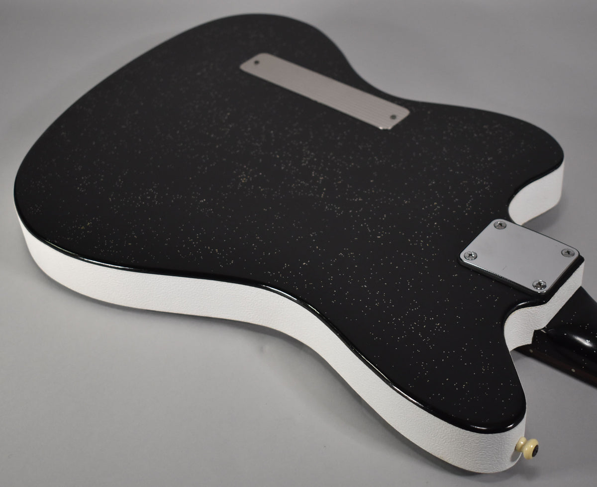 The guitar's black sparkle back and sides are visible, with a white textured binding and chrome neck plate and string-through ferrule cover.