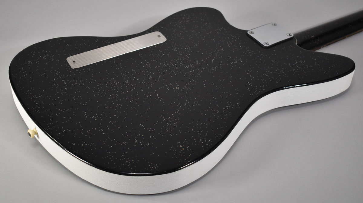 The guitar's black sparkle back and white textured sides are visible, with a chrome neck plate and string-through-body ferrule.