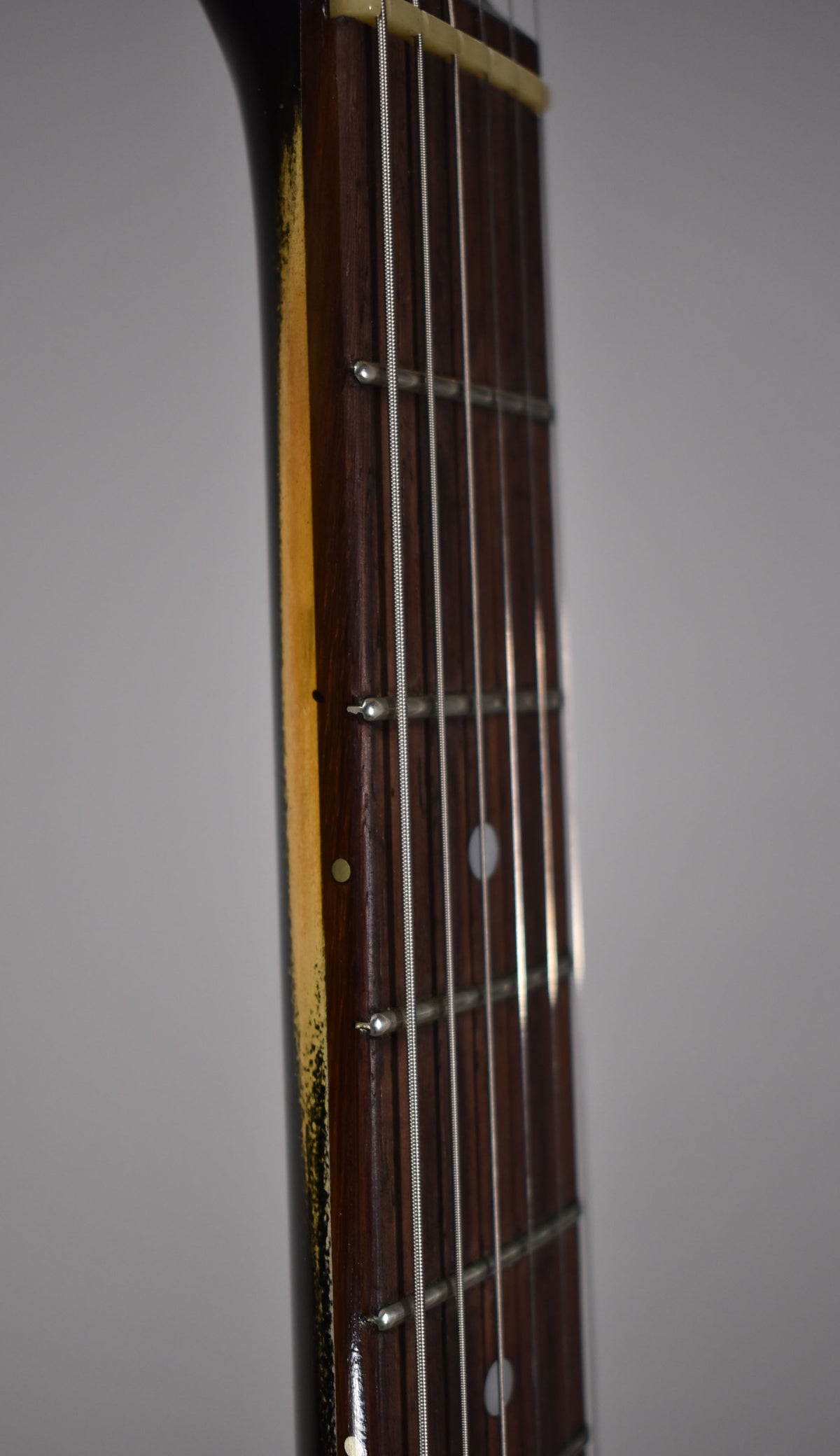 Close-up of the guitar's dark rosewood fretboard with white dot inlays, showing a cream binding and light fret wear.
