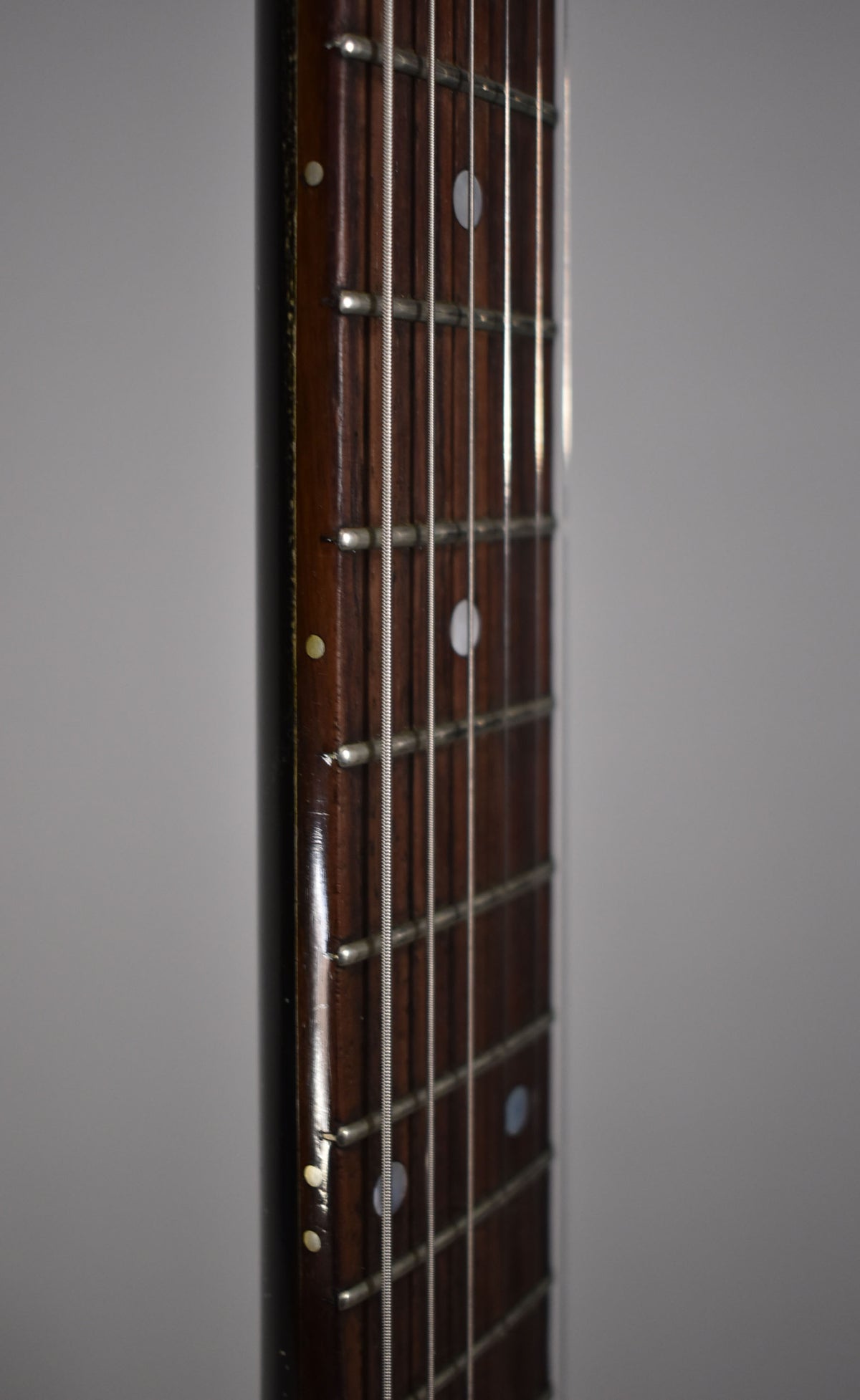 Close-up of the guitar's dark rosewood fretboard with white dot inlays, showing frets and strings from a side angle.