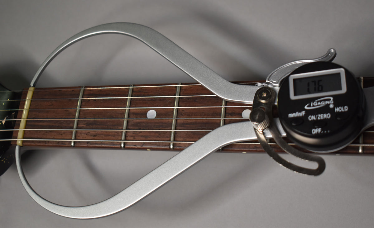 Close-up of the guitar's dark brown fretboard with white dot inlays, measured by a silver digital caliper displaying "1.76".