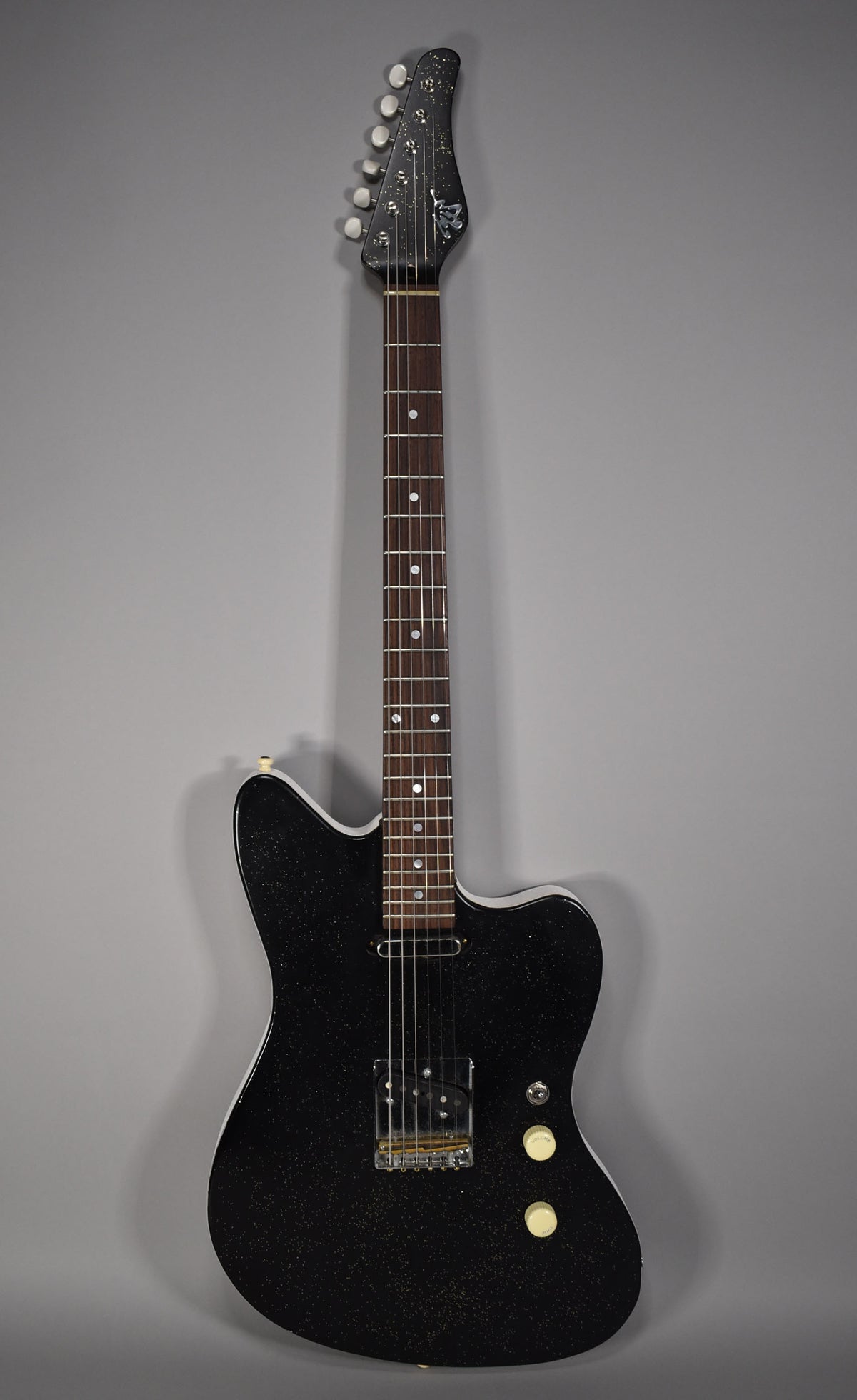 Full-length view of a black sparkle electric guitar with a single bridge humbucker, two cream knobs, and white binding.