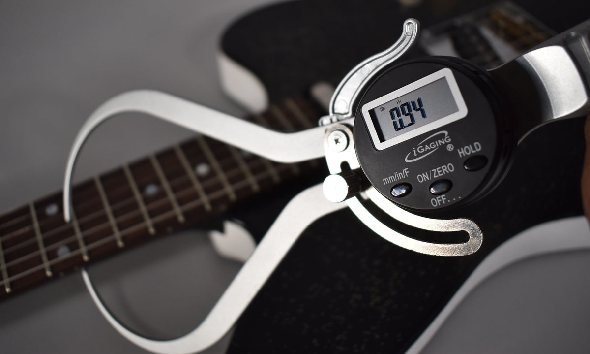 A digital caliper measures the Jitlada's black sparkle body, showing a 0.94 reading, with the fretboard visible in the background.