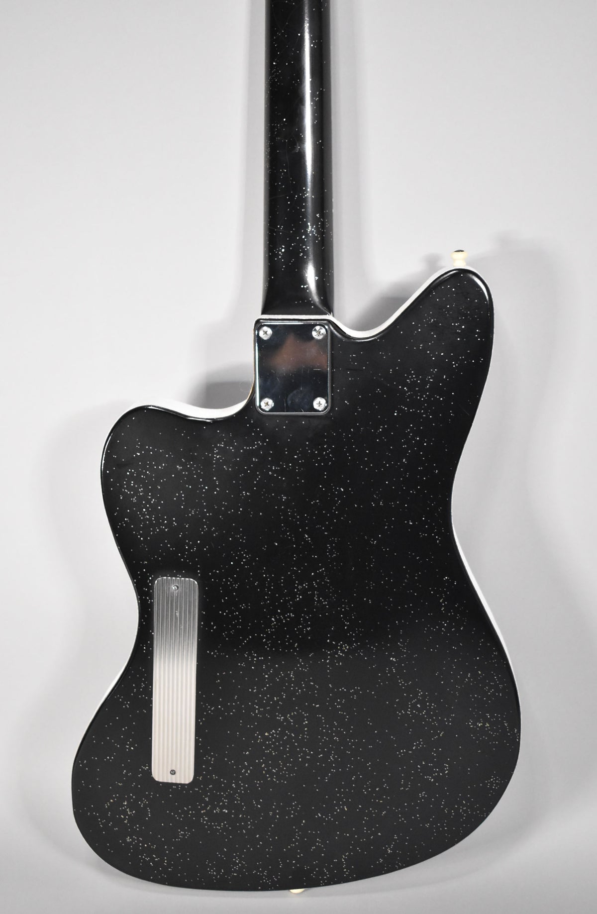 The guitar's black sparkle back, with a chrome neck plate and ribbed control cavity cover, is angled slightly left.